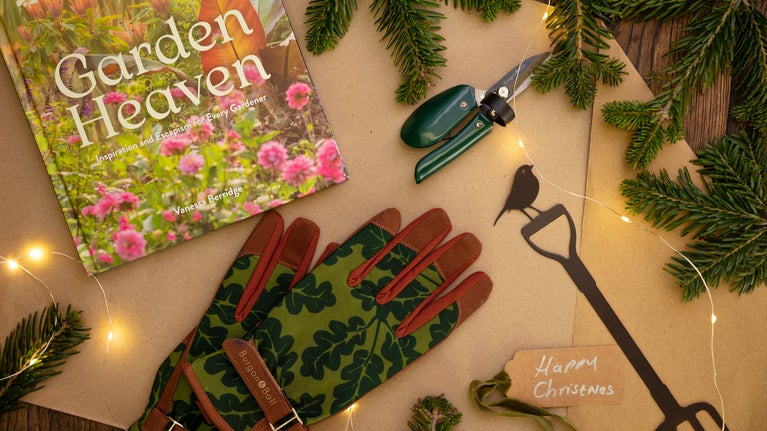 Fairy lights intertwined with gardening gloves, a book and gardening fork